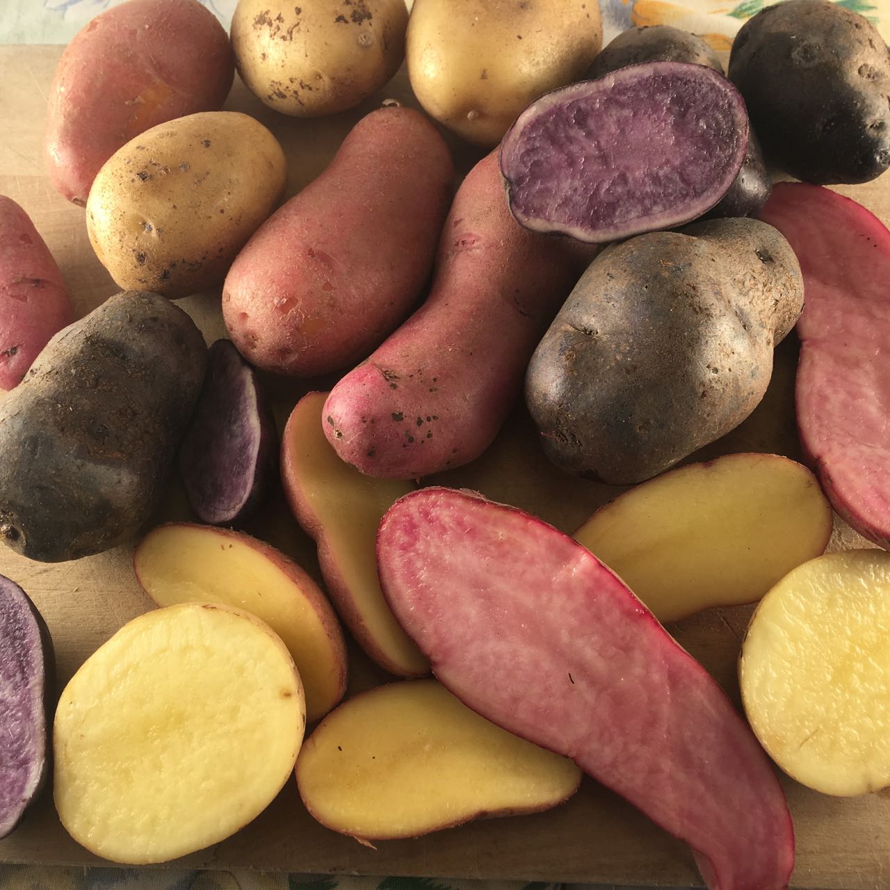 Une variété de pommes de terre présentées sur une table, dont des pommes de terre entières et coupées en deux. Les pommes de terre sont jaunes, rouges et violettes, présentant différentes couleurs et textures.